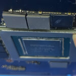 Close-up of a graphics card with a memory module being inserted; a finger holds the edge of the module.