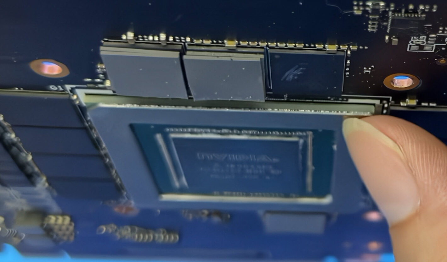 Close-up of a graphics card with a memory module being inserted; a finger holds the edge of the module.