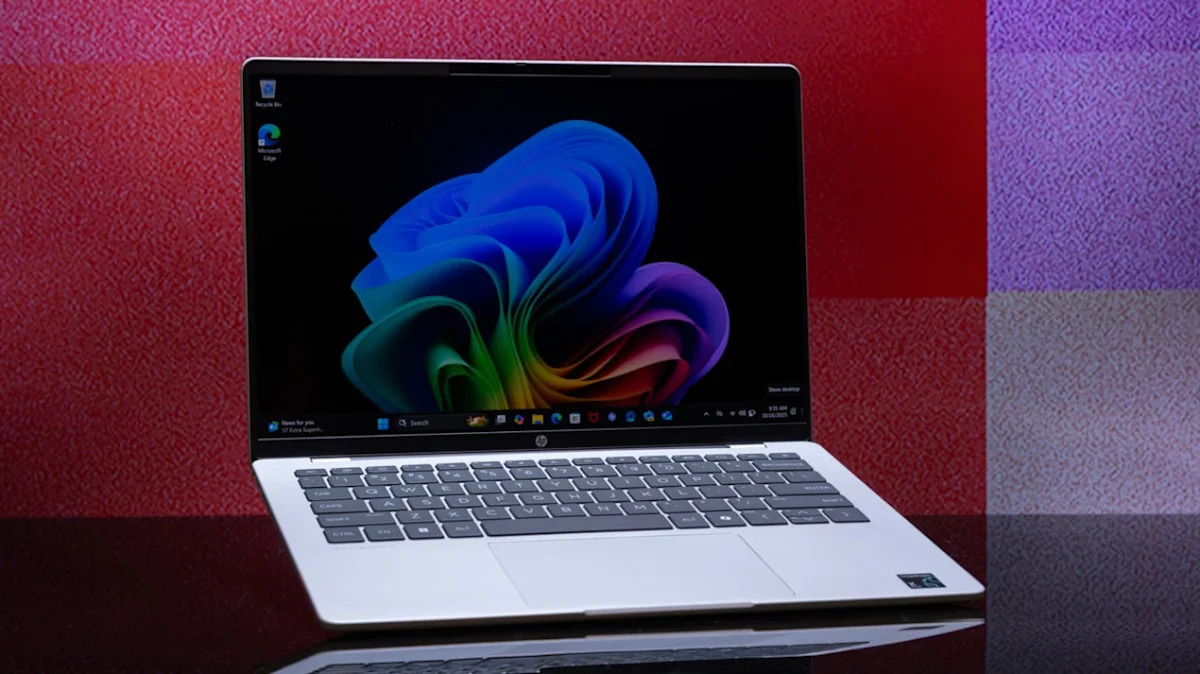 Open silver laptop displaying a vibrant abstract blue-to-green wallpaper on a glossy black surface against a red and purple checkered background.