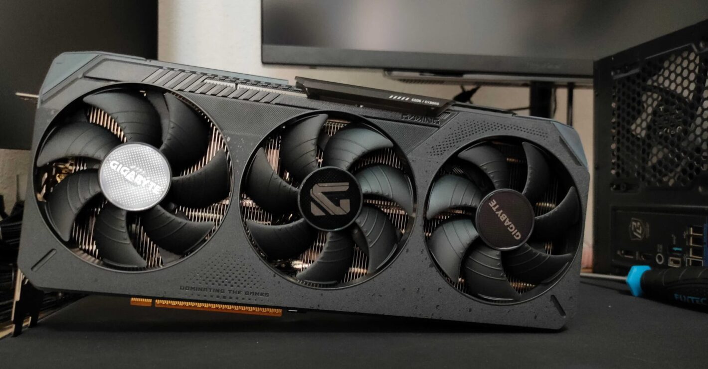Triple‑fan graphics card from Gigabyte installed in a PC, visible heatsink and case side panel in the background, slogan 'Dominating the Games' on the card.