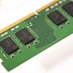 Green RAM module with a gold edge connector and black memory chips visible on a green PCB, seen at an angle.