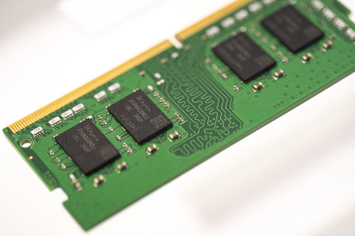 Green RAM module with a gold edge connector and black memory chips visible on a green PCB, seen at an angle.